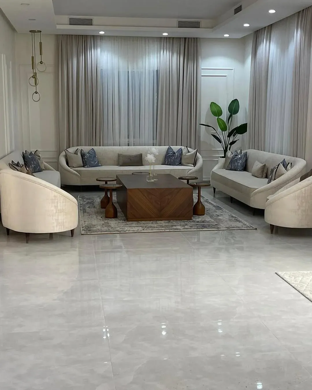 طقم كنب مجلس كريمي من كنبات بظهر مقوّس ملتف وأرجل خشب مخروطة موزعة حول طاولة في صالة